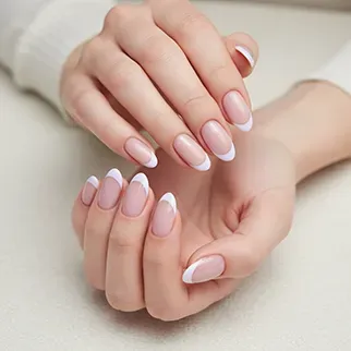 A close-up of serene hands showing a meticulously applied, classic French manicure with almond-shaped nails on a soft white background.